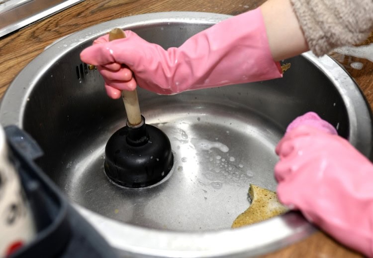 Woman clearing clogged kitchen drain